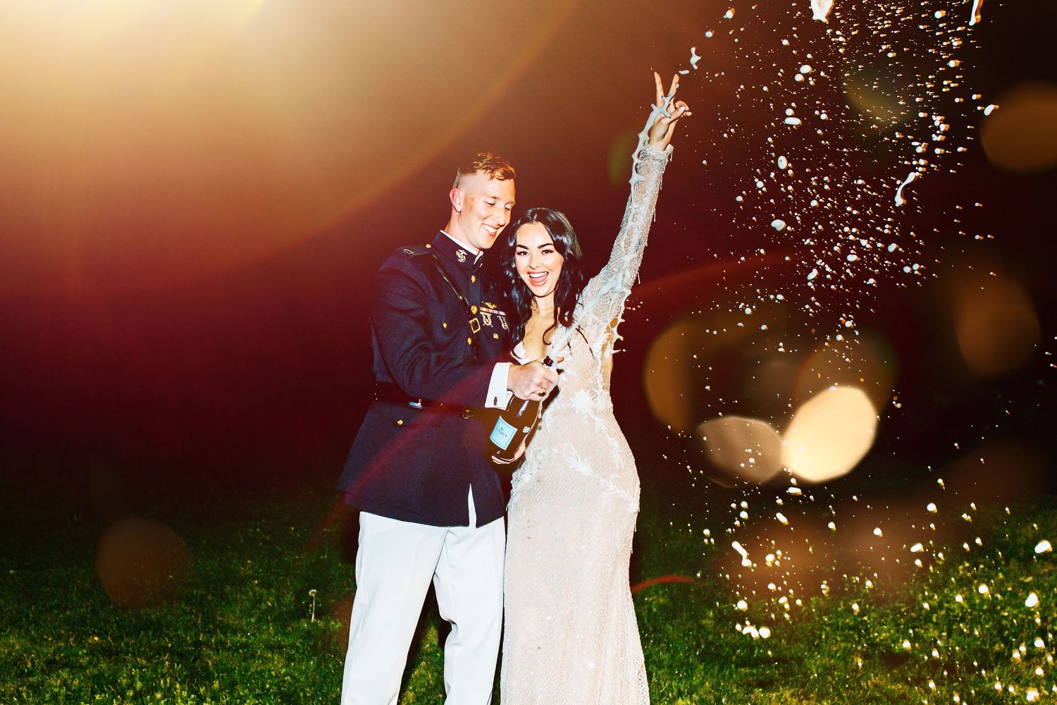 A couple in wedding attire celebrates with sparklers in an outdoor evening setting with glowing bokeh effects.