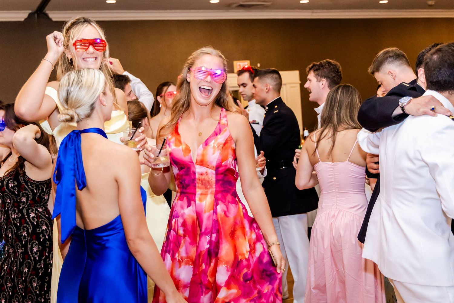 Wedding guests in colorful dresses dancing and celebrating at reception party.