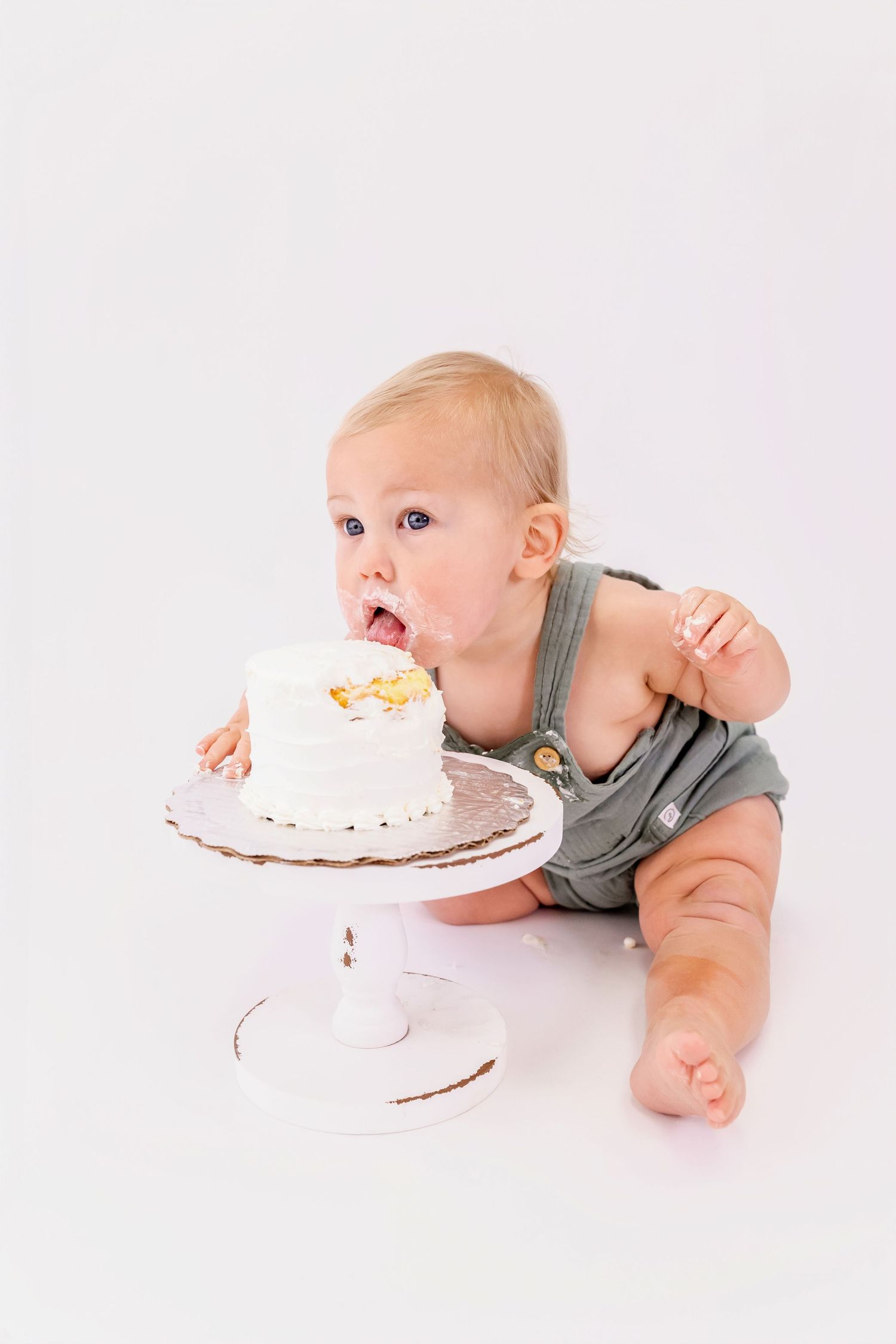 A sequence of three photos showing a baby in gray overalls eagerly diving face-first into a white frosted cake.