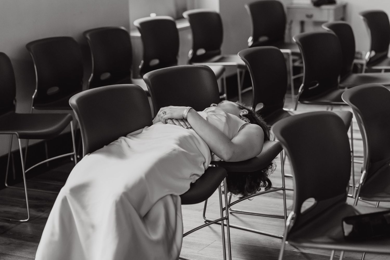 Empty chairs arranged in rows in a classroom or conference room with white walls and fluorescent lighting.