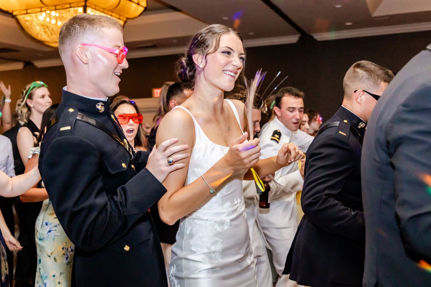 Wedding guests dancing energetically on a crowded dance floor under warm lighting at an elegant reception venue.
