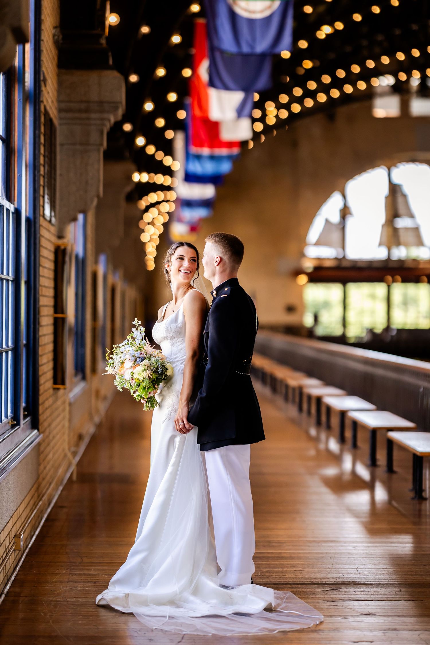 A romantic wedding couple poses in an elegant hallway with string lights and flags creating a warm ambiance.