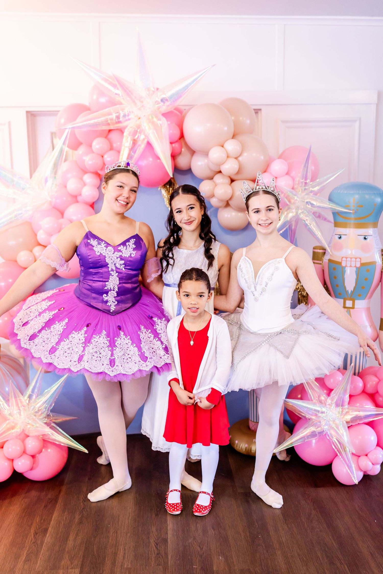 Young dancers in tutus and ballet costumes posing against pink balloon decorations.