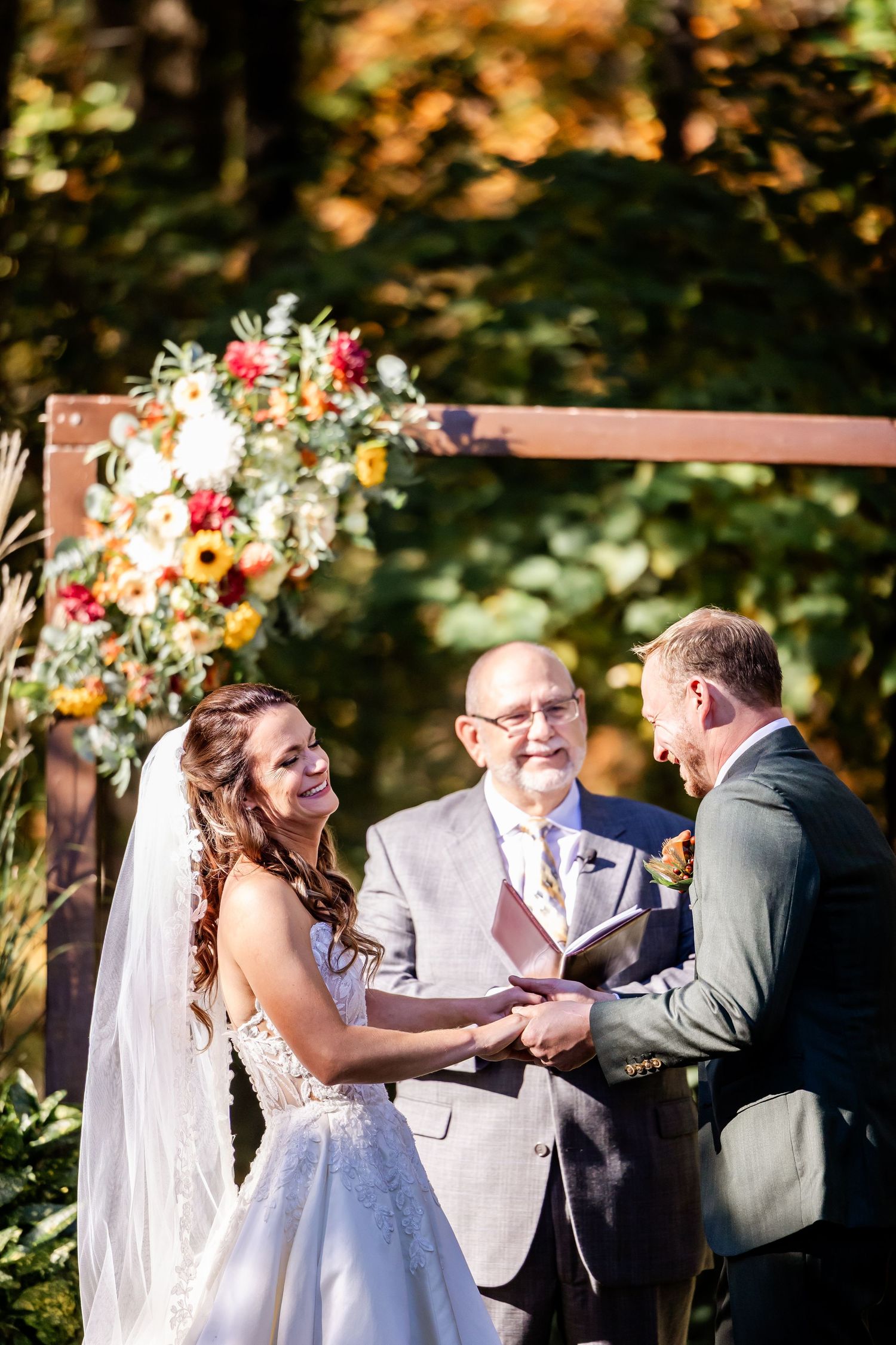 Wedding ceremony taking place outdoors with couple exchanging rings under autumn foliage.