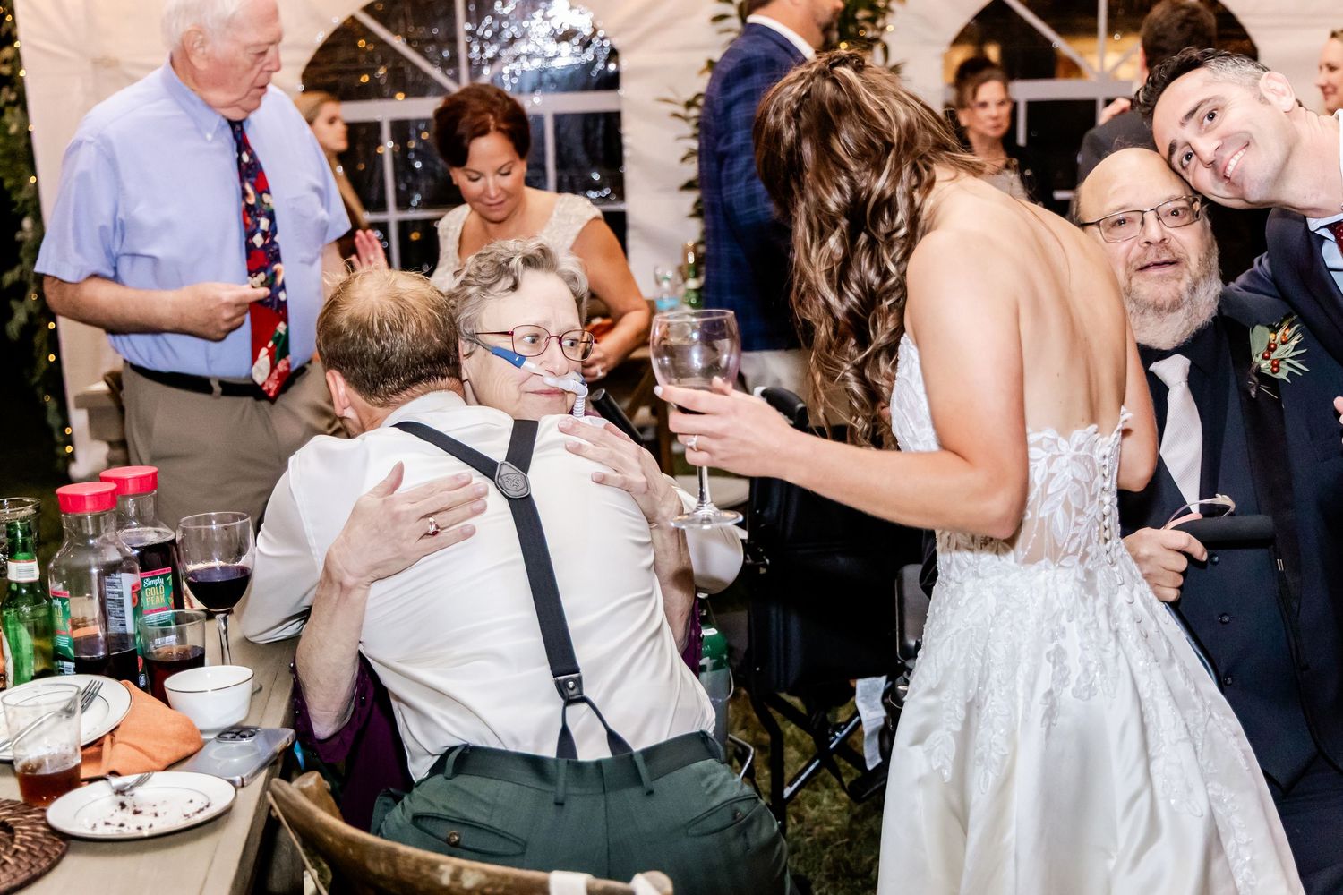 Wedding guests mingling and celebrating during the reception under white tent lighting.
