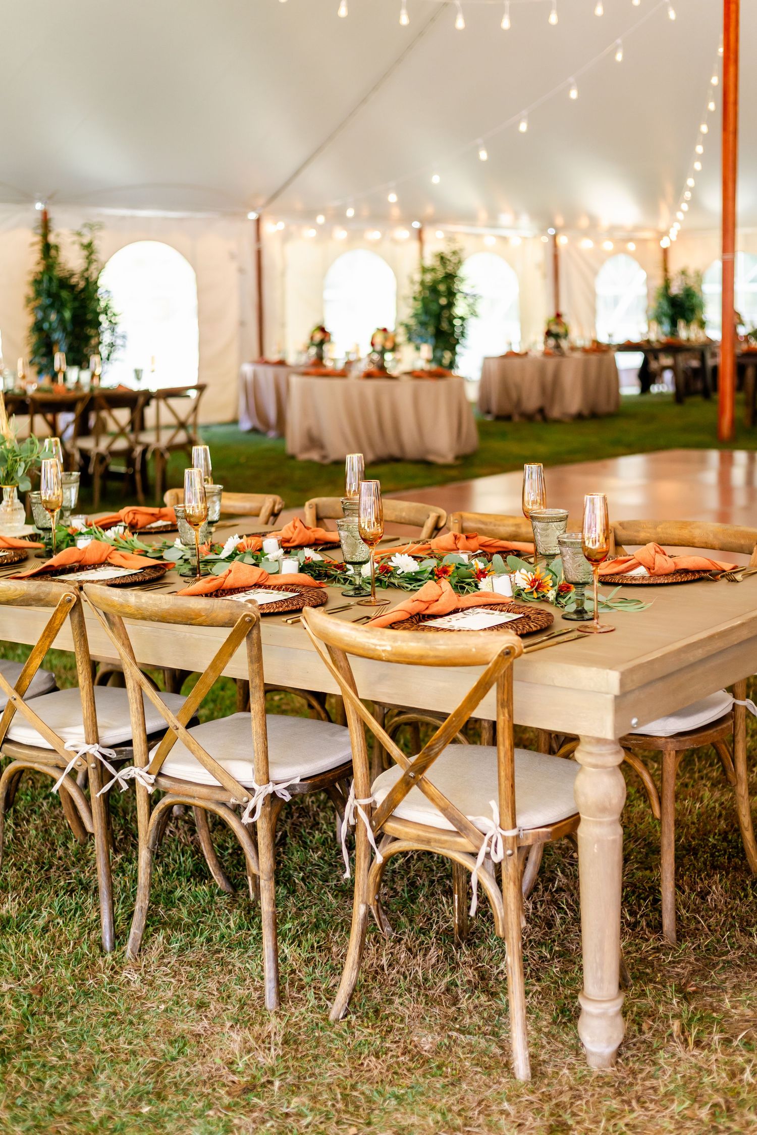 Elegant table settings under a white tent with string lights and natural decor.