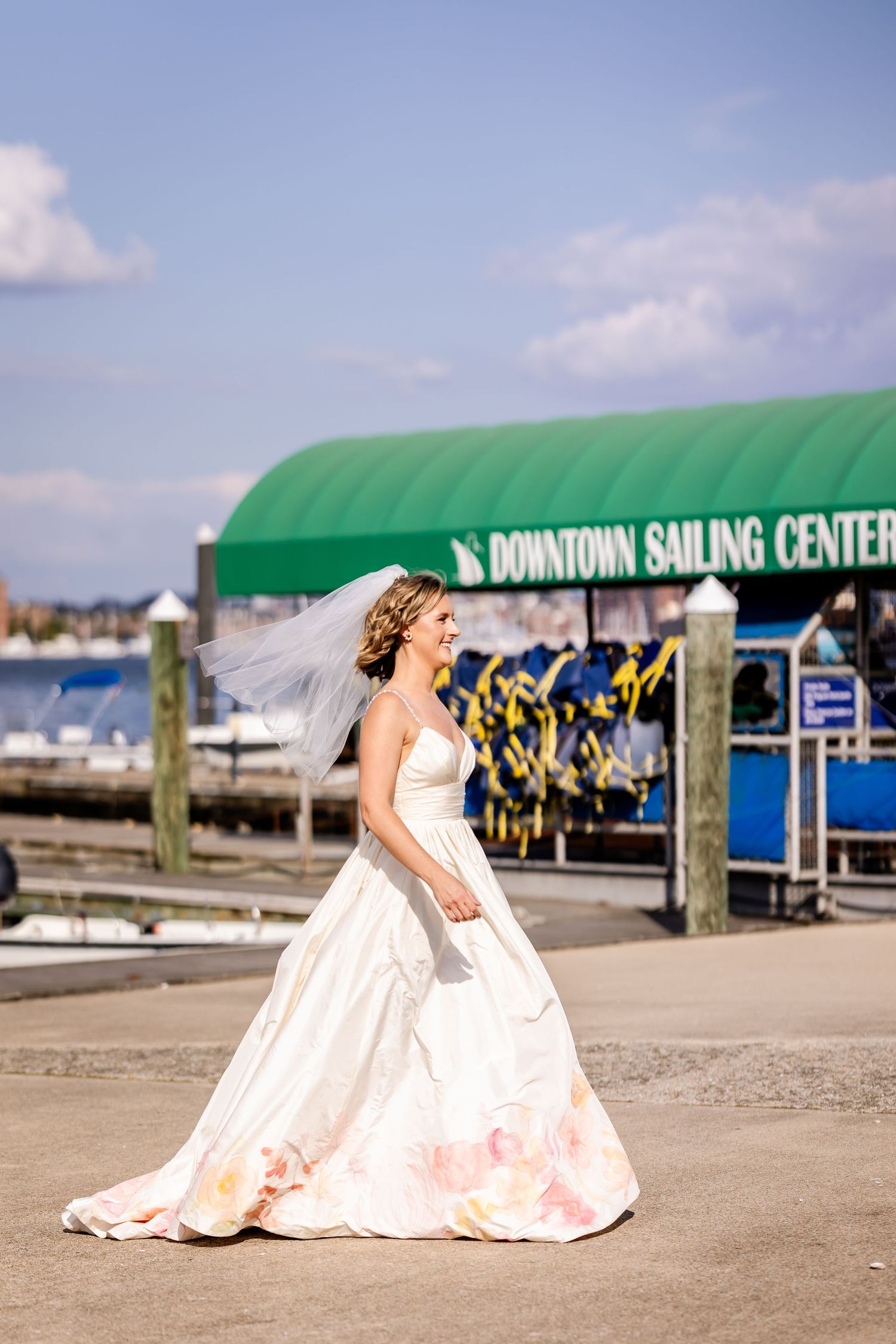 A white wedding dress flows elegantly against a marina backdrop with a green awning for Downtown Sailing Center.