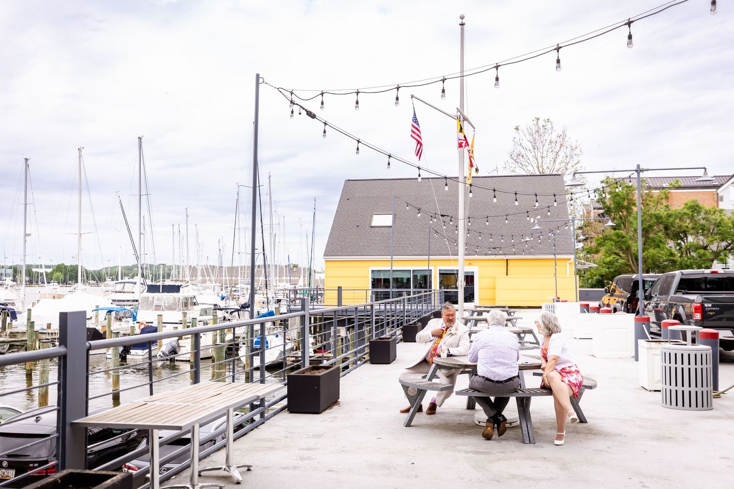 Outdoor marina dining area with string lights and yellow building in the background.