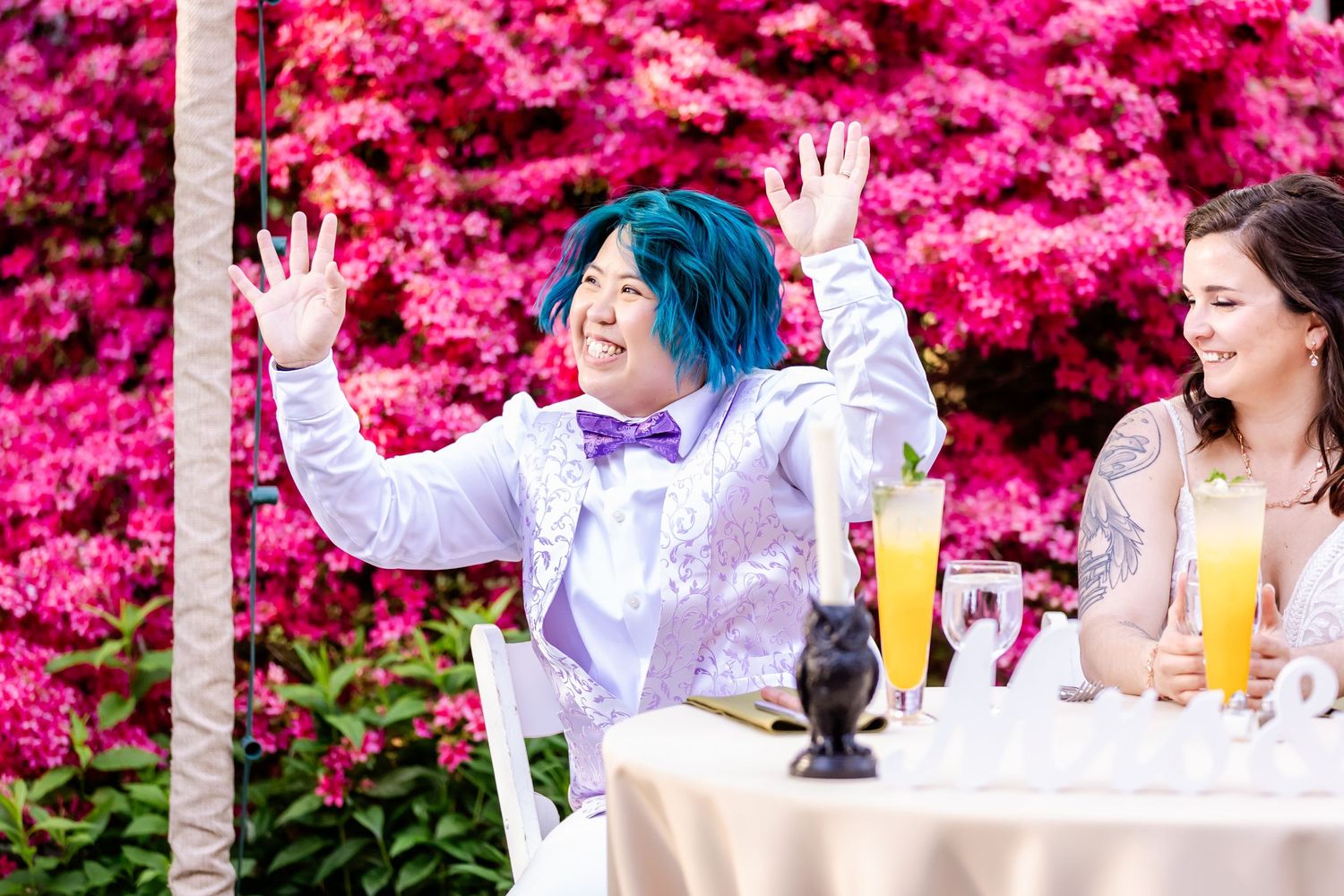 A cheerful celebration against vibrant pink flowering bushes with refreshments on a white table.