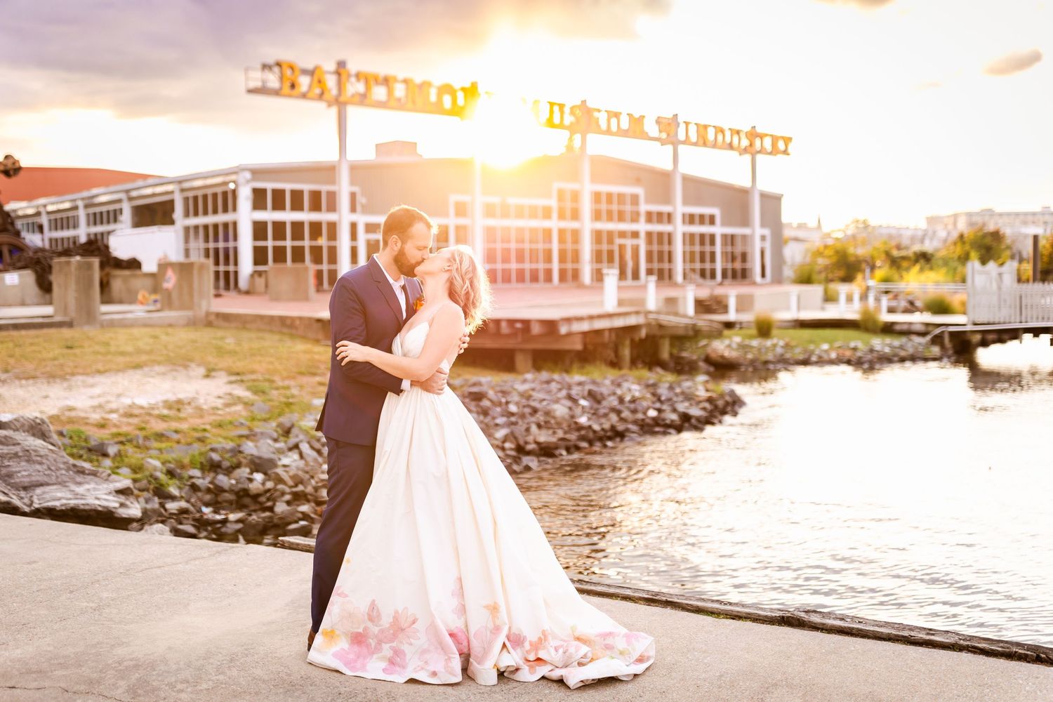 Romantic wedding photo at sunset with couple standing by a waterfront restaurant.
