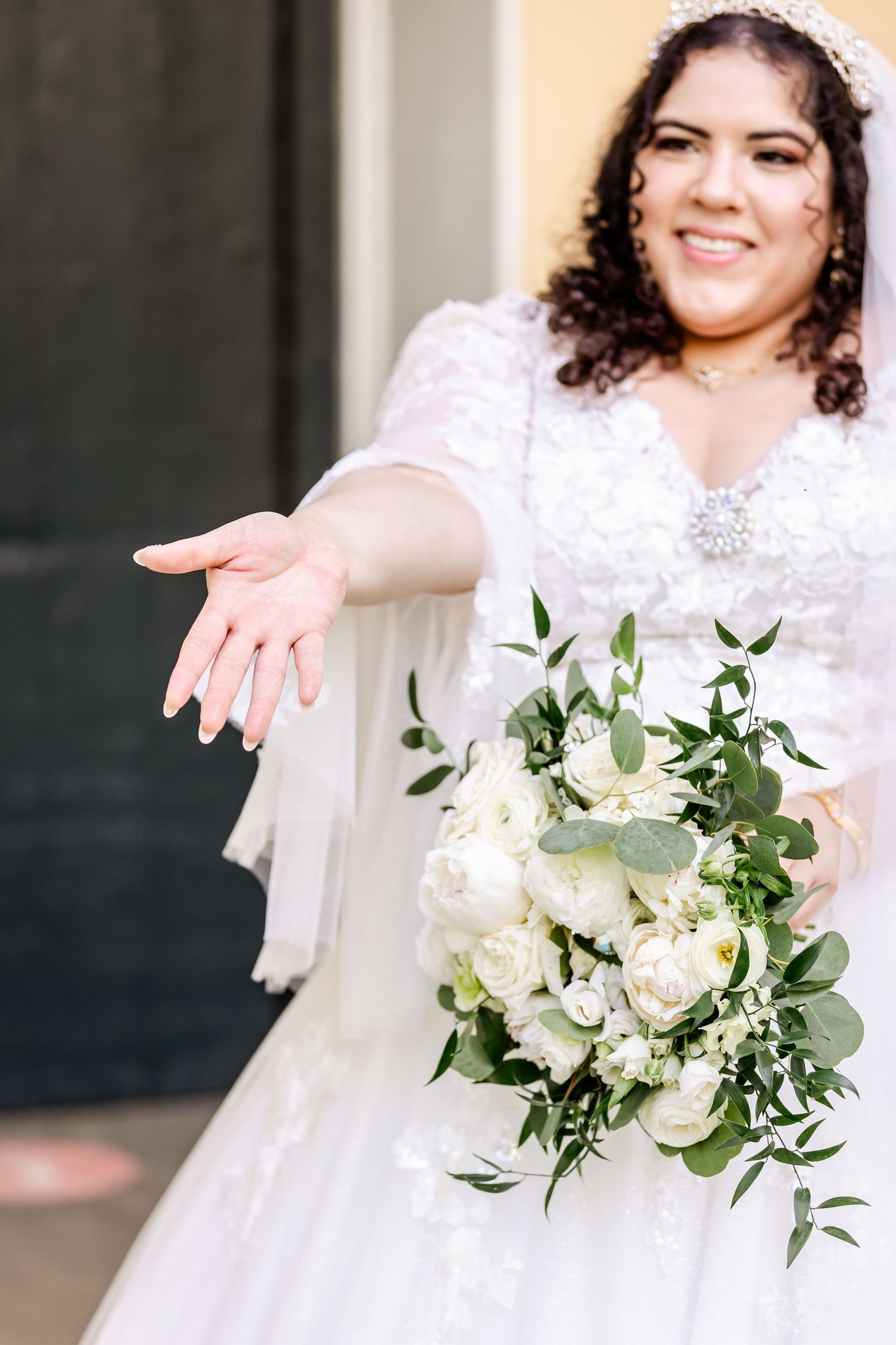 Beautiful white wedding bouquet of roses and greenery held by someone in a lace wedding gown.