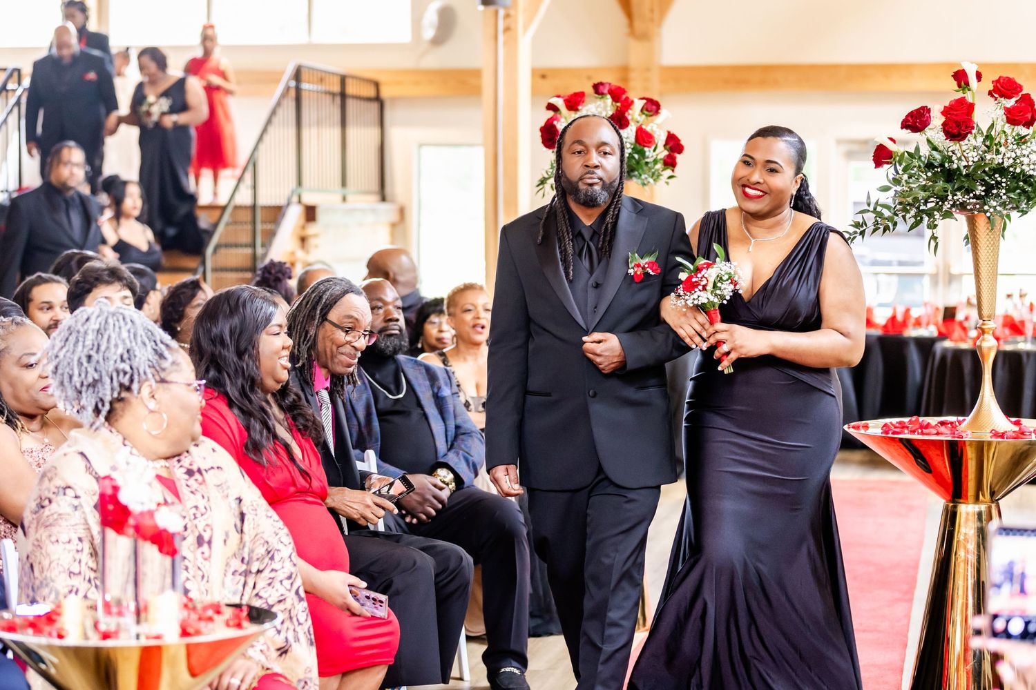 Wedding guests watch attentively during a ceremony with red roses and elegant decor.