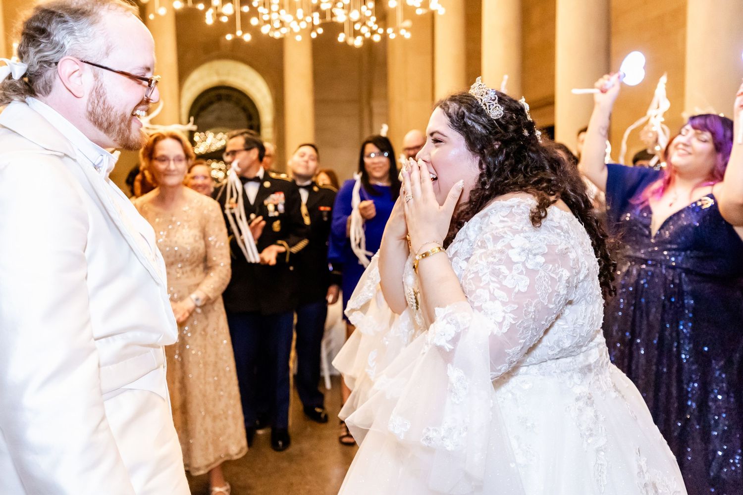 Emotional wedding moment captured in an elegant venue with chandelier lighting and stone columns.