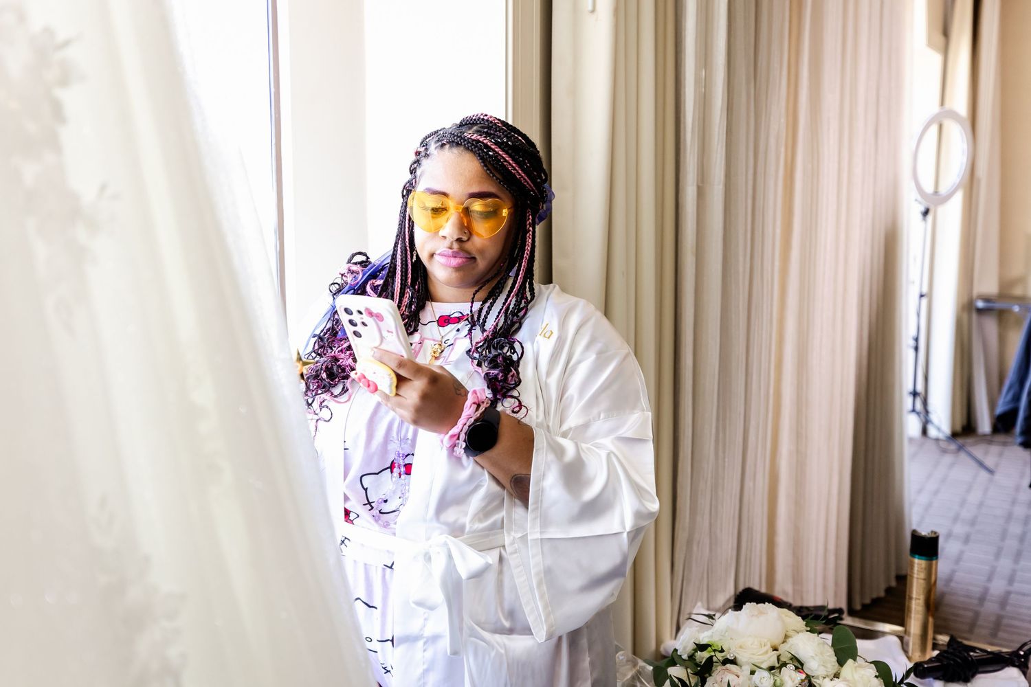Person in white robe and Hello Kitty print holding a phone in natural window light.