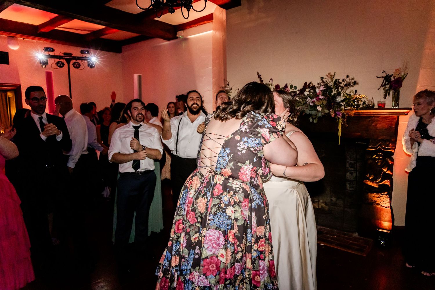 Wedding reception guests dancing and celebrating in a venue with red mood lighting.