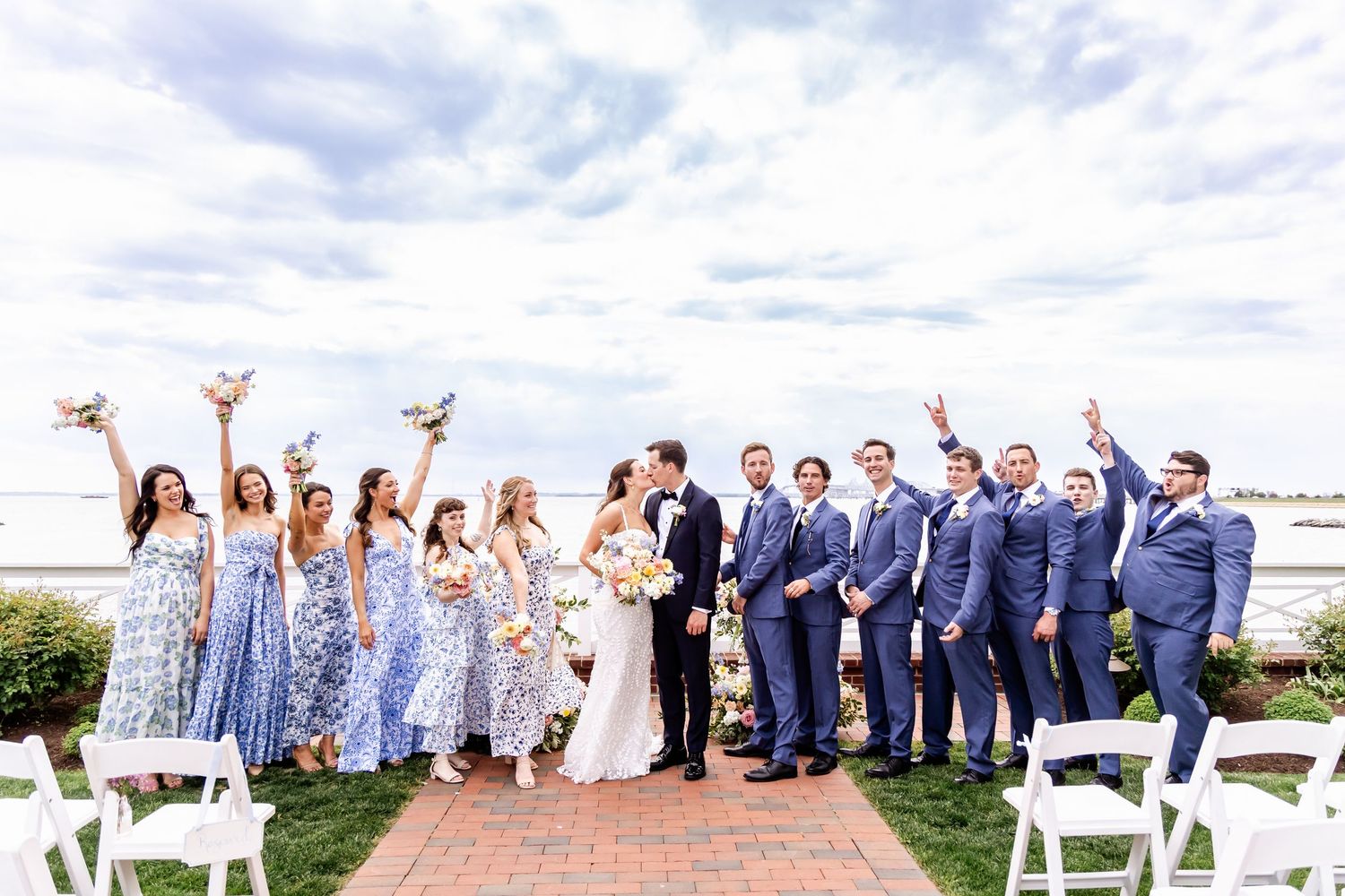 Wedding party poses for group photos on a grassy lawn under cloudy skies.