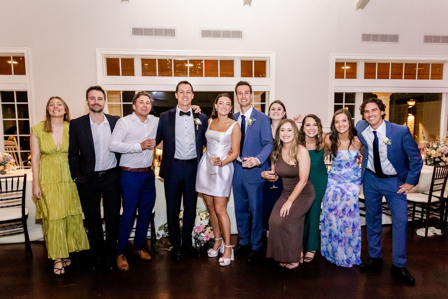 Wedding party members in navy suits and floral dresses pose together for formal group photos.