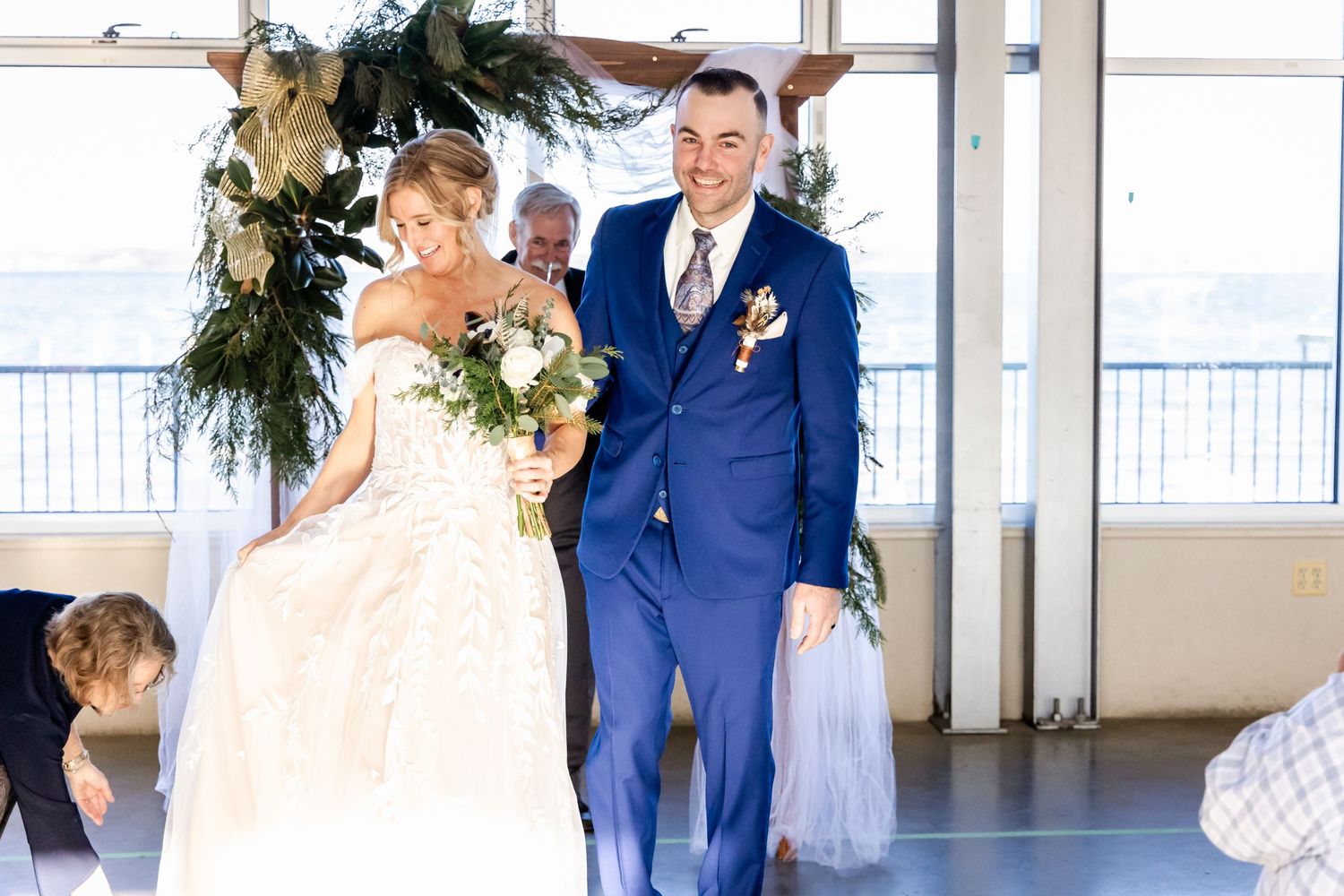 Wedding ceremony in bright indoor venue with floral arch and guests in attendance.