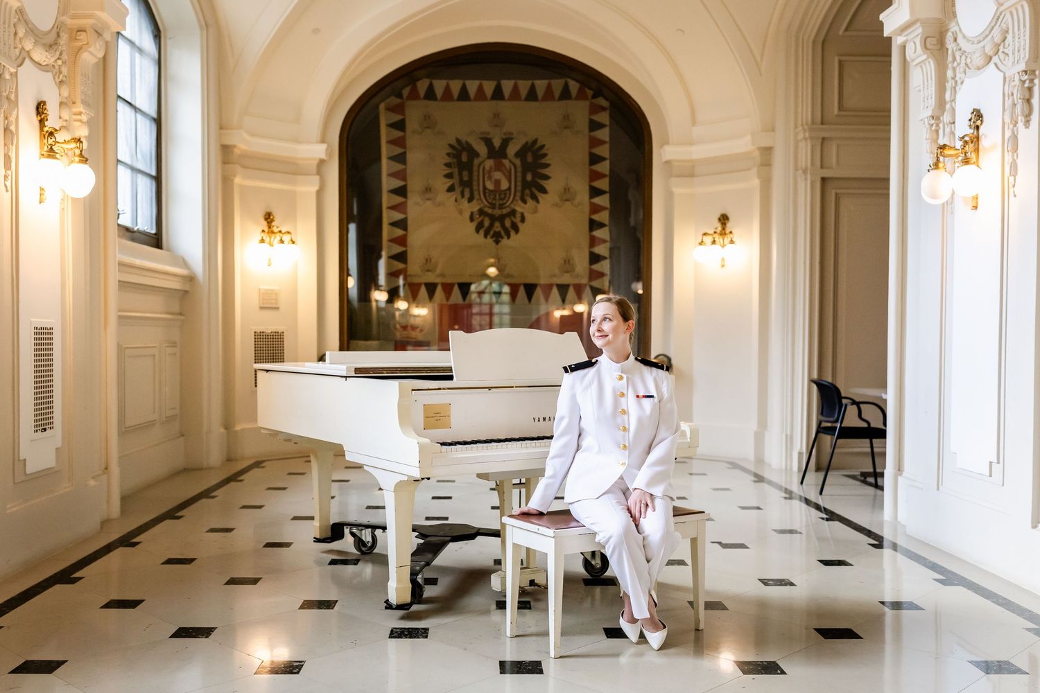 An elegant white grand piano sits in a regal room with ornate walls, checkerboard floor, and golden sconces.