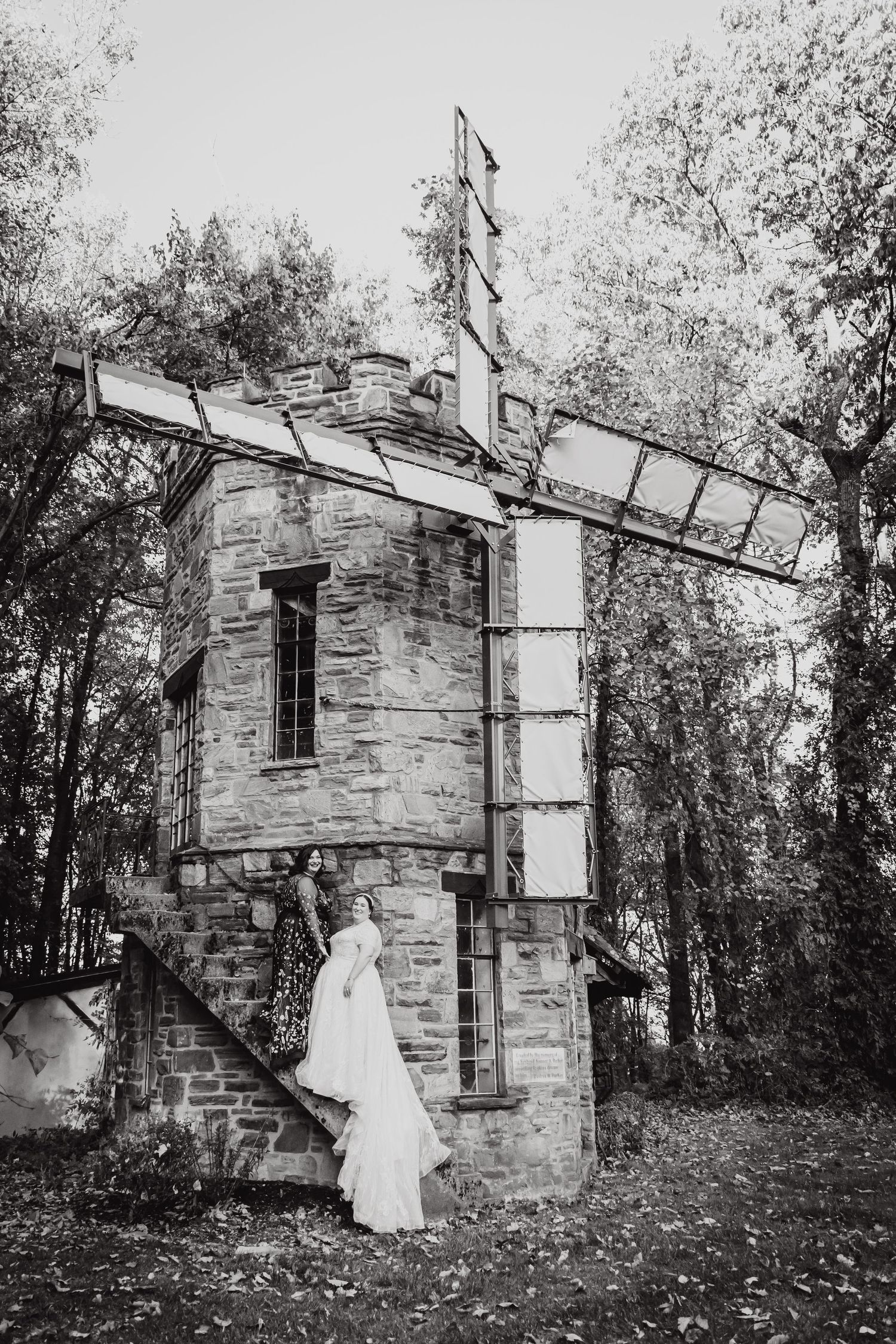 A vintage stone tower in the woods with a flowing white dress cascading down its side in black and white.