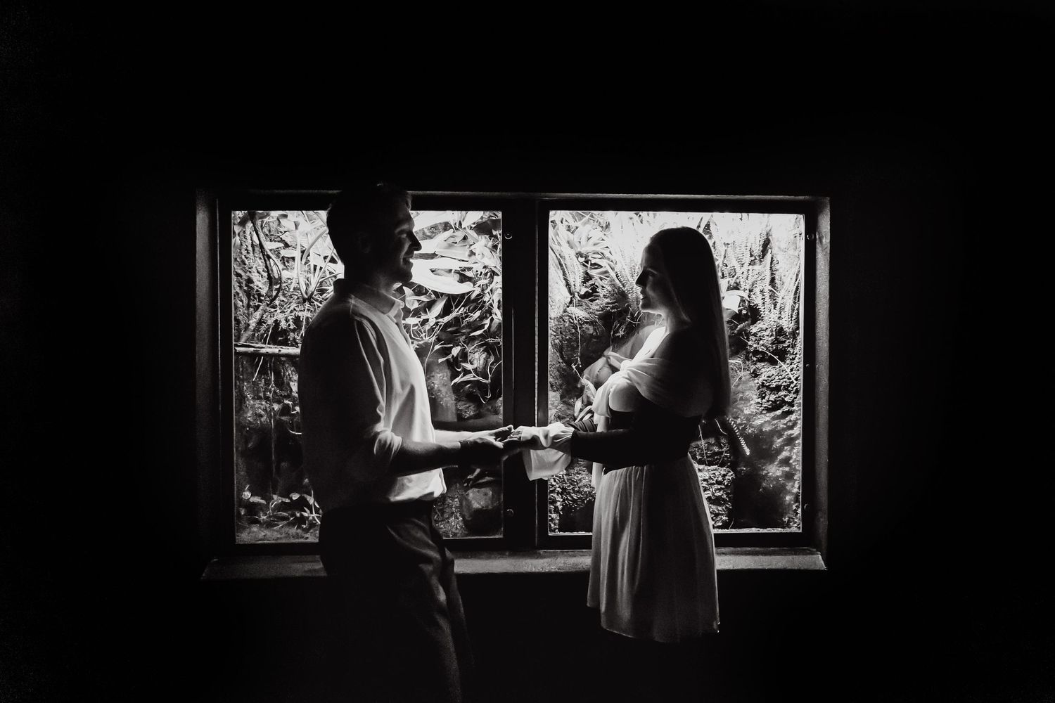 A silhouetted couple stands in front of a window having an intimate conversation in black and white.