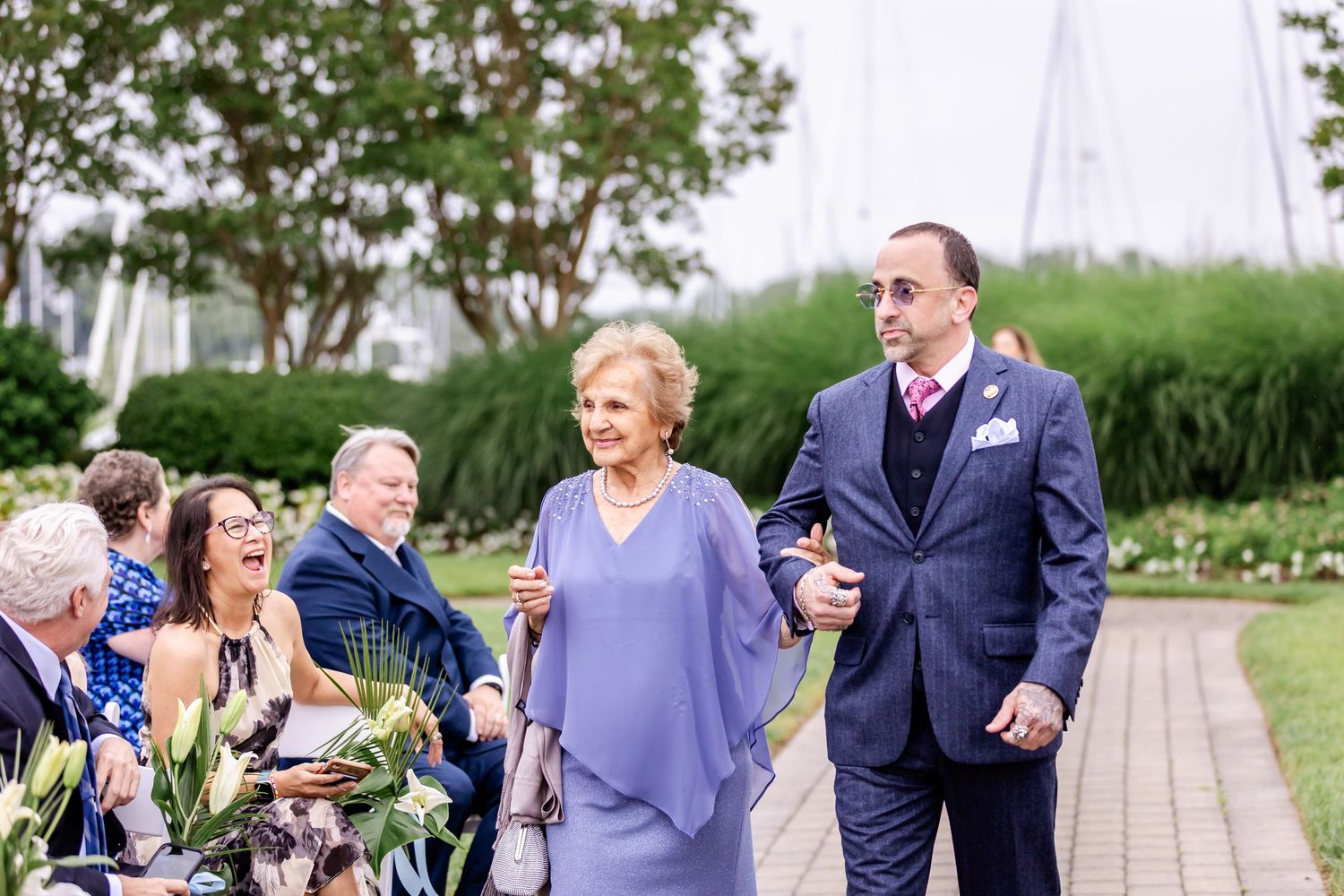 Wedding party members walk together on a garden path during an outdoor celebration.
