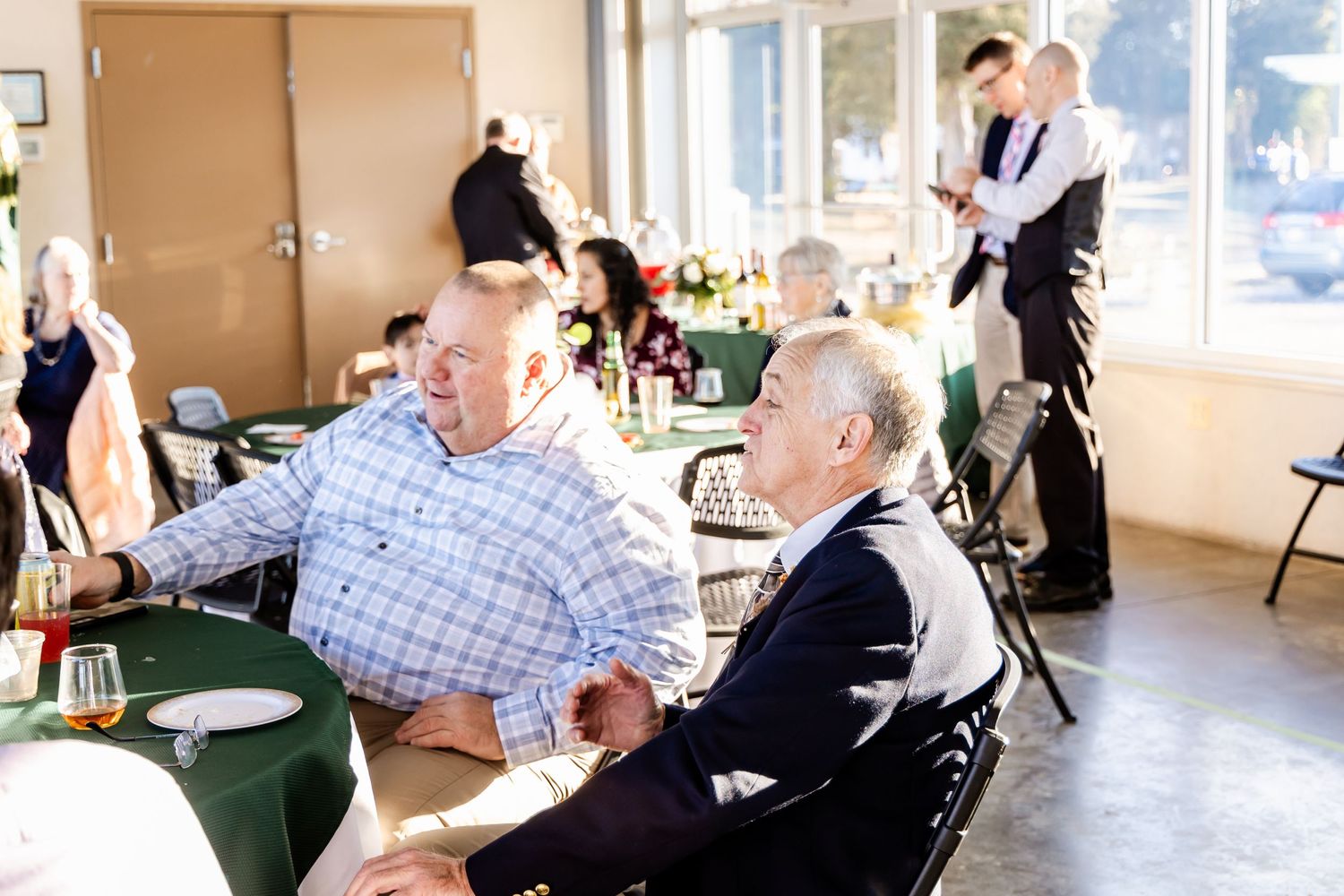 Wedding reception guests seated at tables while server attends in background.