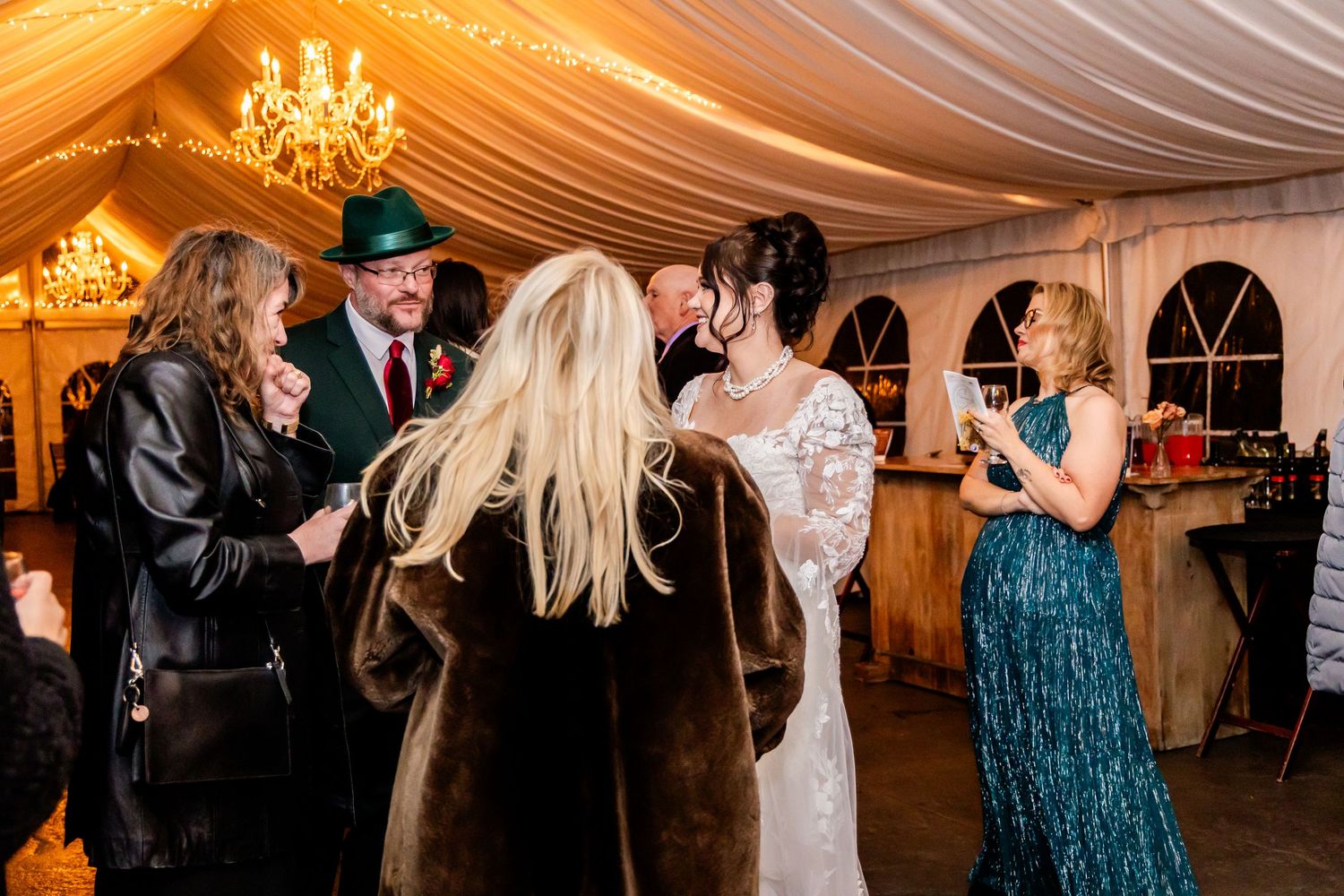 Wedding reception guests dancing and celebrating under warm lighting in a tent venue.