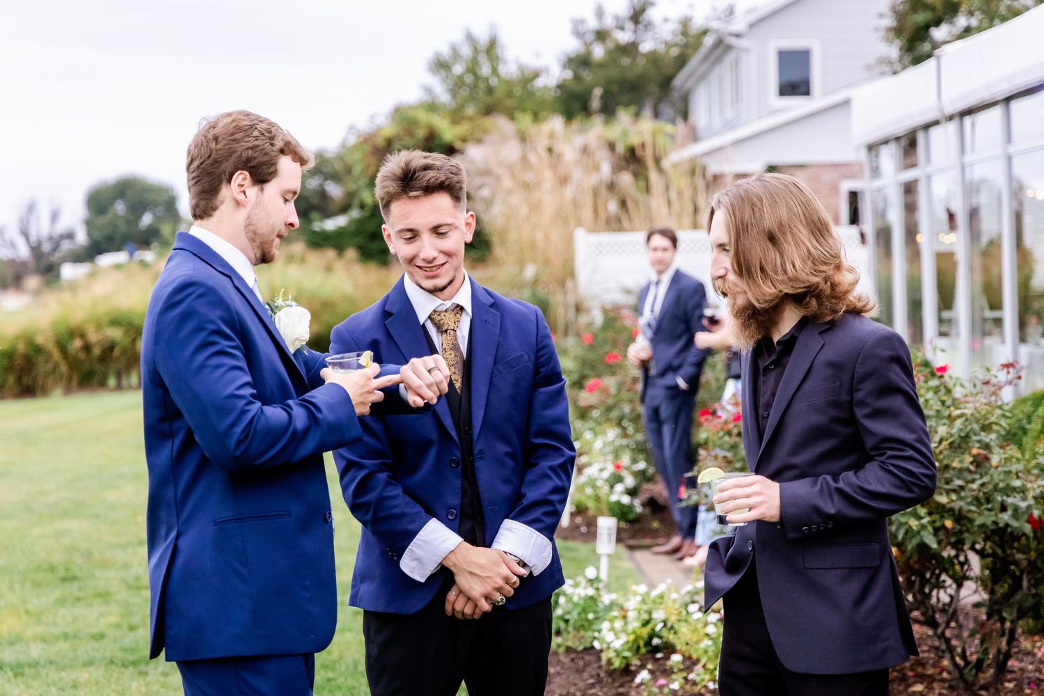 Three people in formal attire share a conversation in a garden setting.