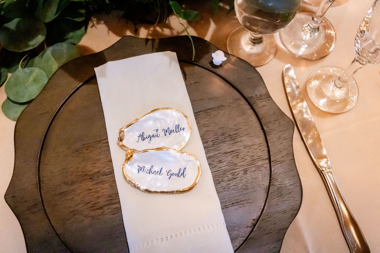Elegant wedding place setting with gold-rimmed agate slice name cards on white napkin atop smoky glass charger plate.