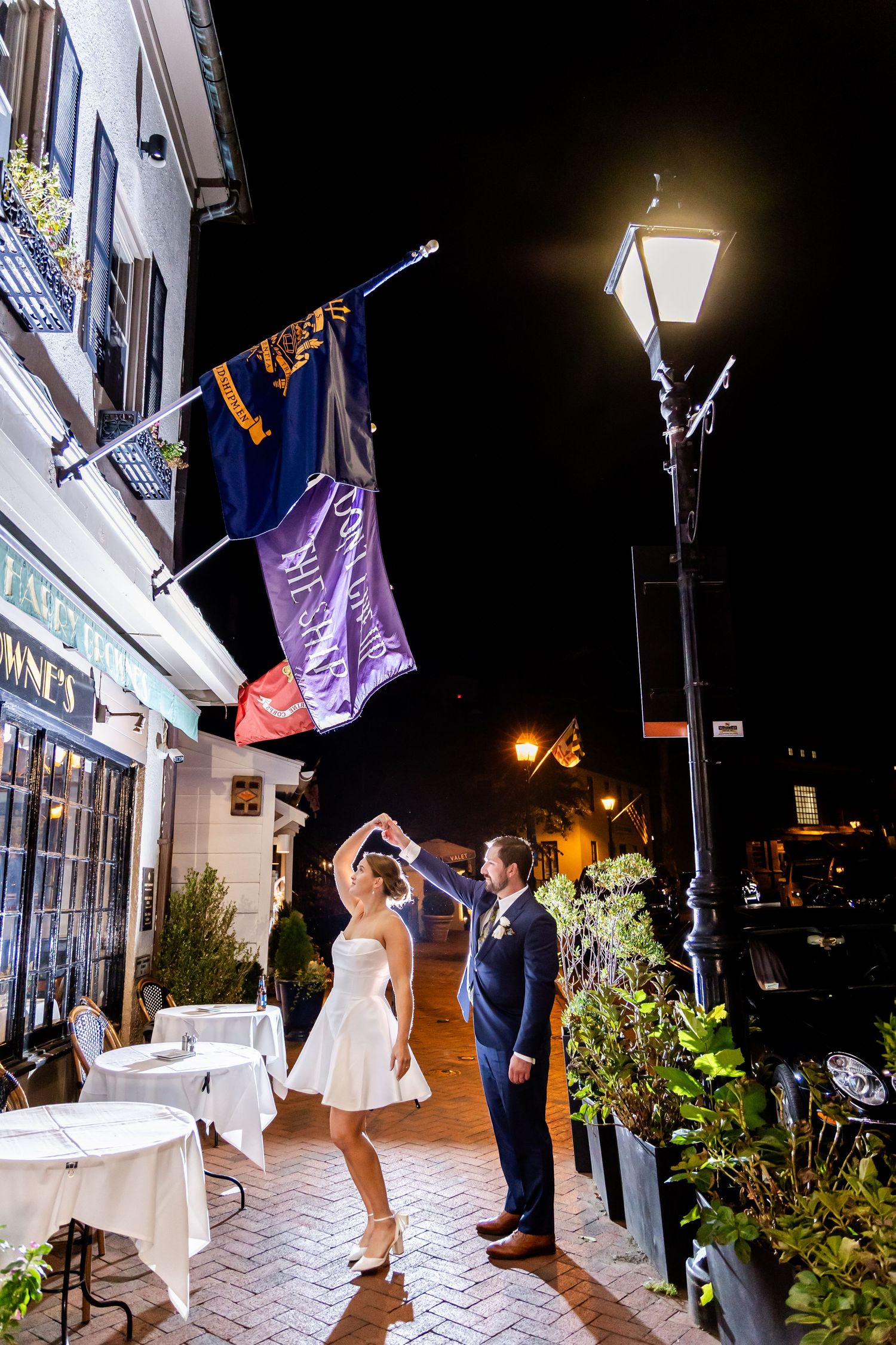 Bride and groom dancing on a charming cobblestone street at night under glowing lamp post and colorful flags.