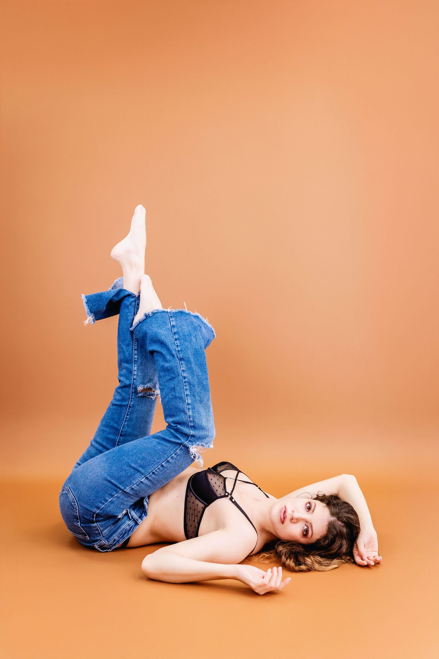 A person in blue jeans lies on an orange backdrop in a series of artistic poses.