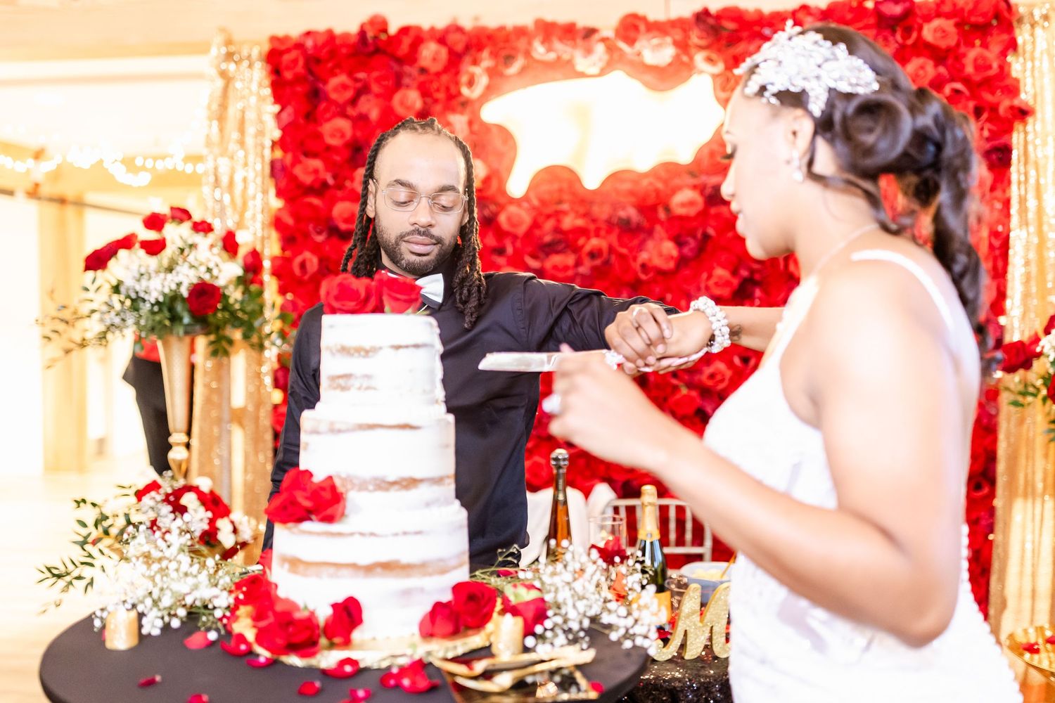 Couple cutting their elegant white wedding cake against a dramatic backdrop of red roses.