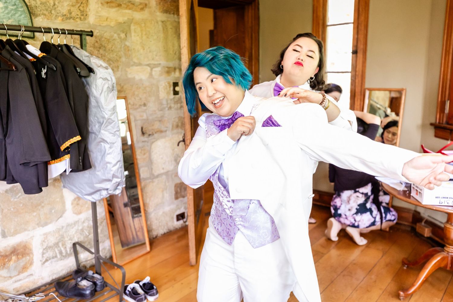Two people share a joyful candid moment in a dressing room with stone walls.