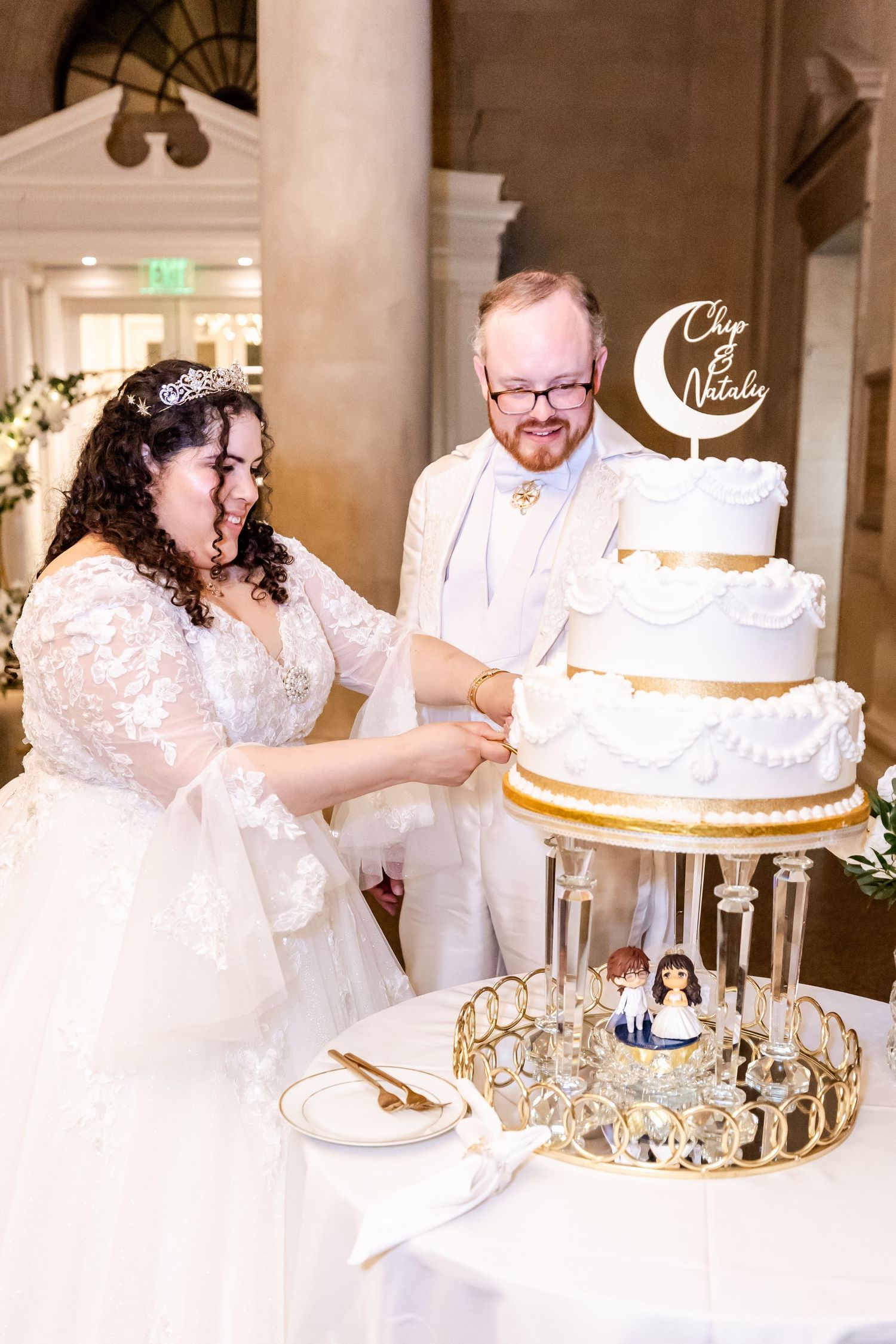 Couple cutting their elegant white and gold tiered wedding cake.
