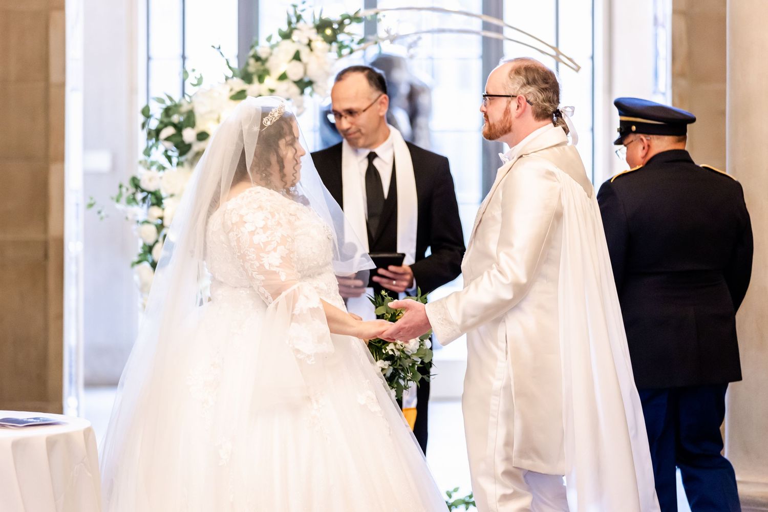 Wedding ceremony with officiant and couple exchanging vows under floral arch.