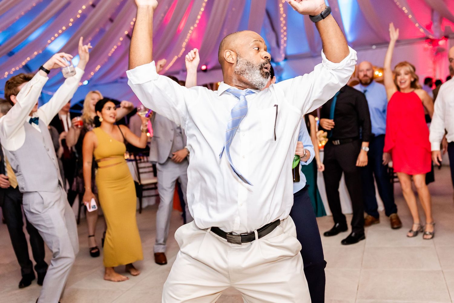 Wedding guest dances enthusiastically with arms raised on the dance floor during a festively decorated reception celebration.