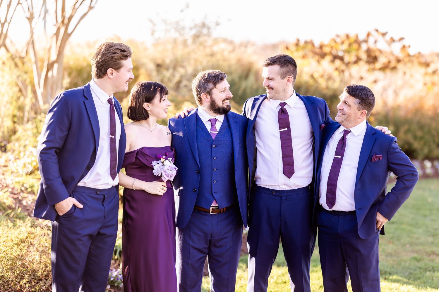 Group laughing together in formal attire against natural garden backdrop at sunset.