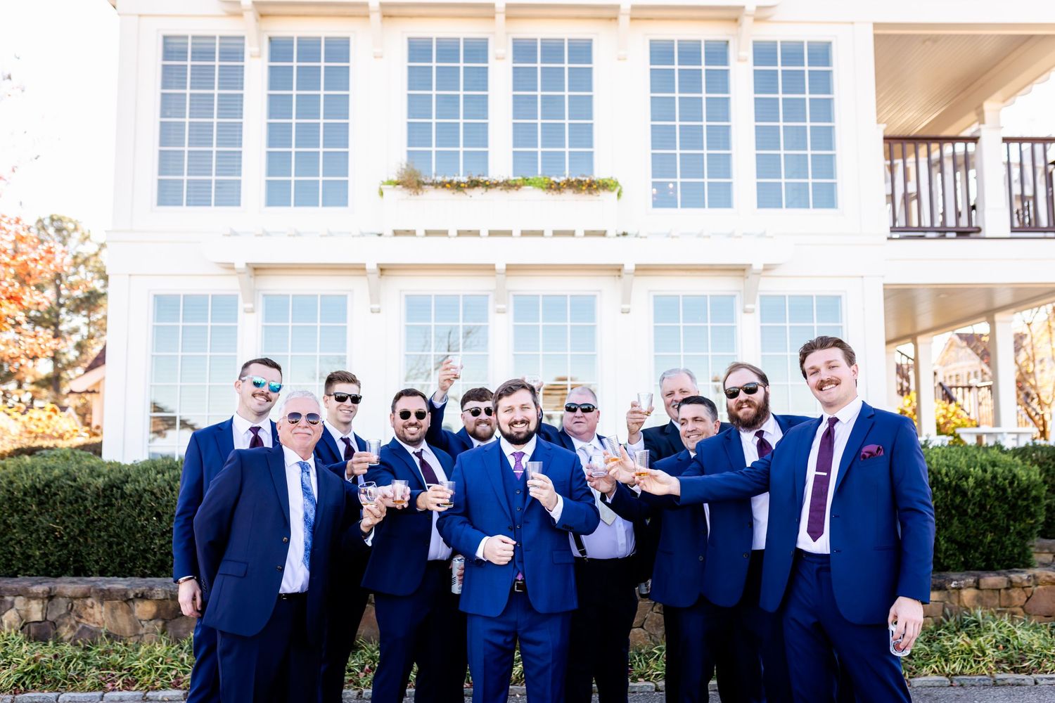 A group in matching navy suits poses together in front of a white colonial style building.