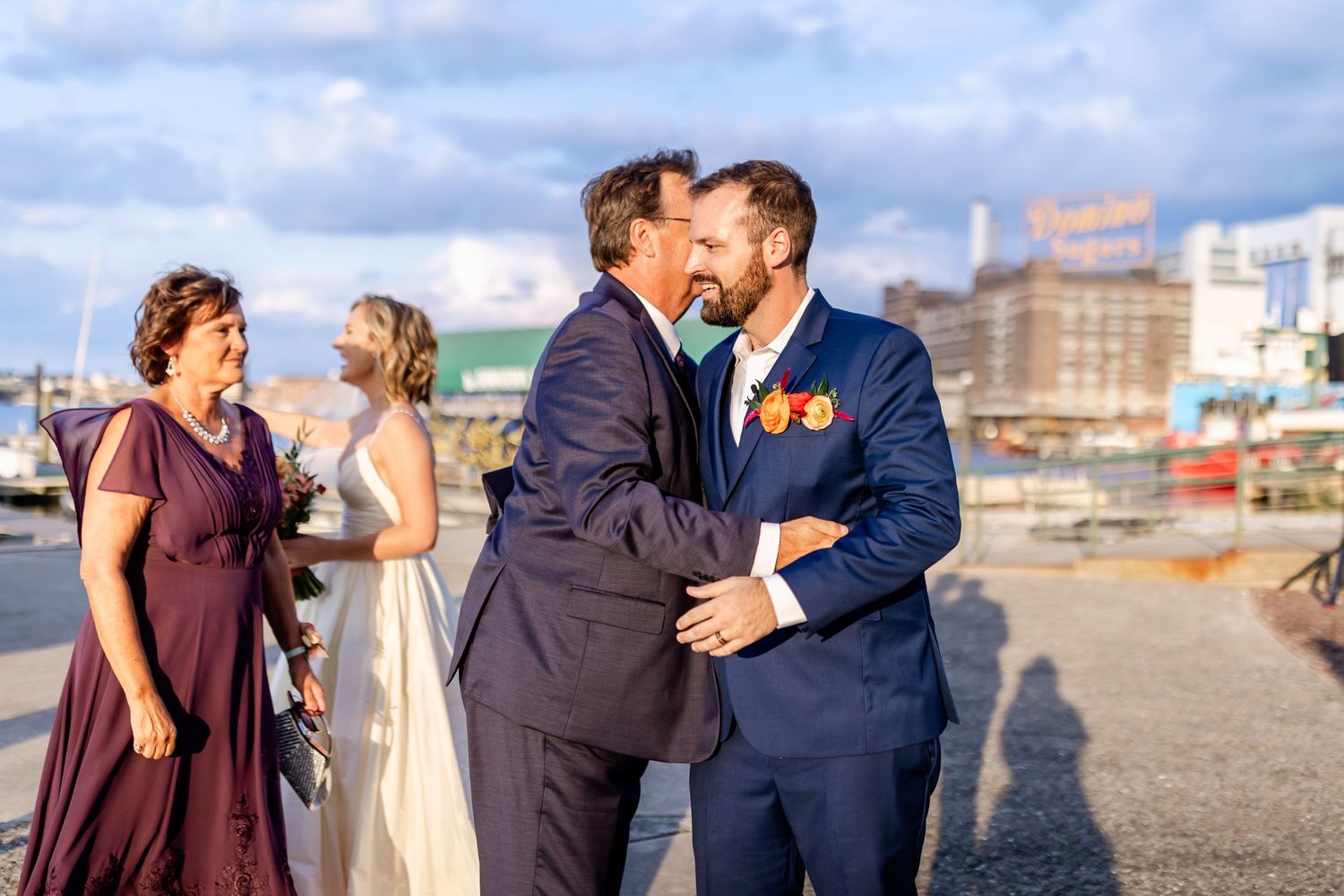 An emotional embrace shared between wedding attendees at a waterfront venue.