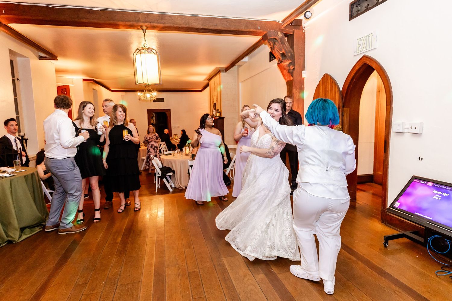 Wedding guests dancing and celebrating in a rustic indoor venue with wooden floors.