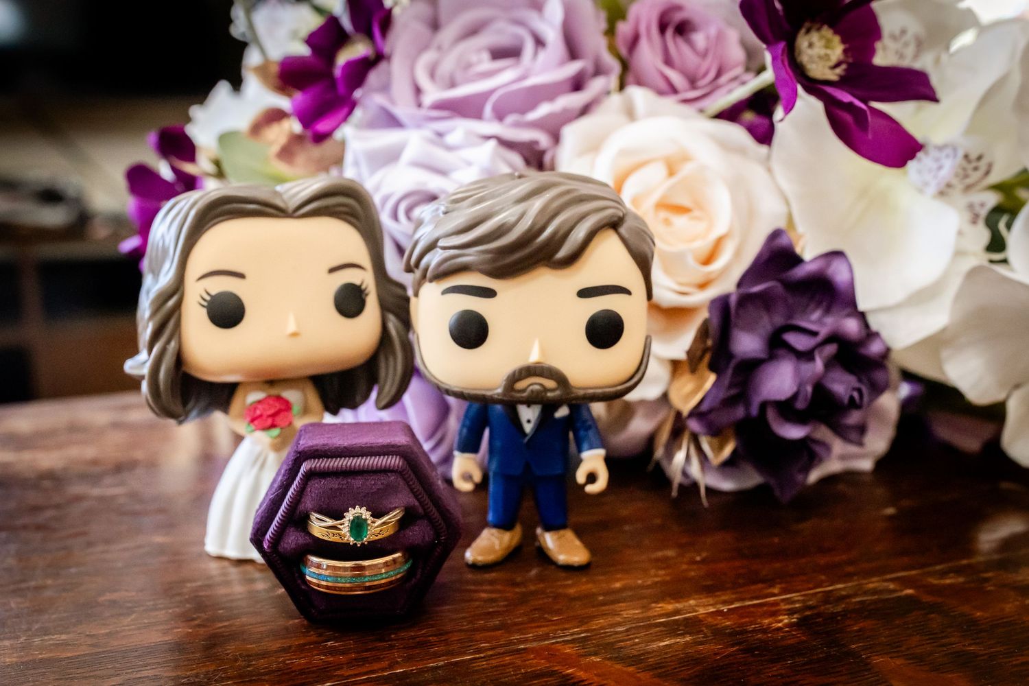 Decorative Funko Pop figures arranged with purple and pink flowers and wedding decor on a wooden surface.