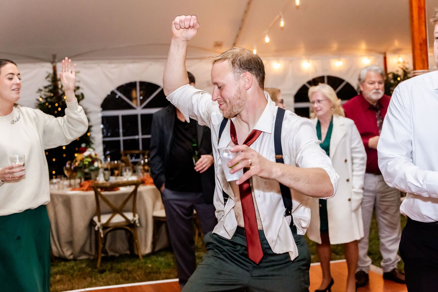 Wedding reception guests dancing and celebrating enthusiastically inside a tent venue.