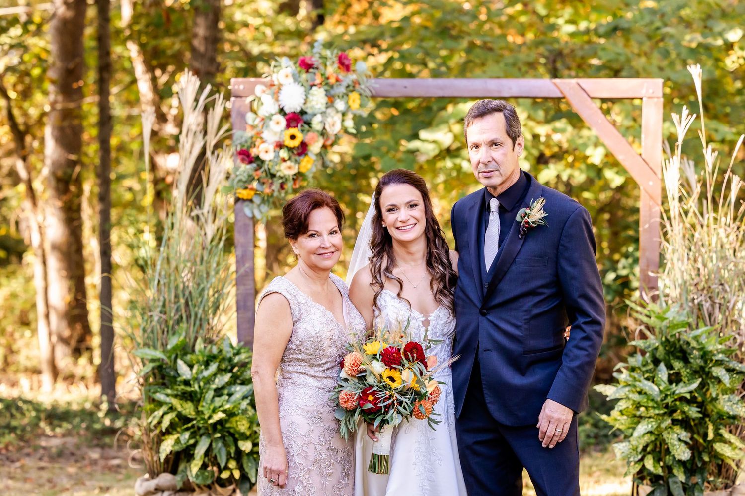 Wedding party members gather for formal photos in a wooded outdoor setting.