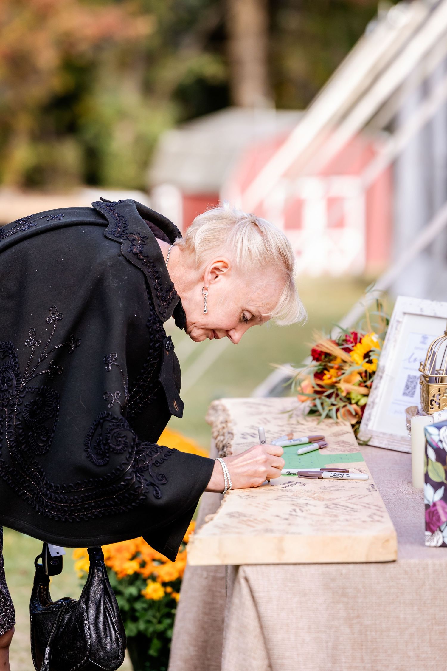 Guest signing book at outdoor wedding reception with sunflowers and decorative table setup.