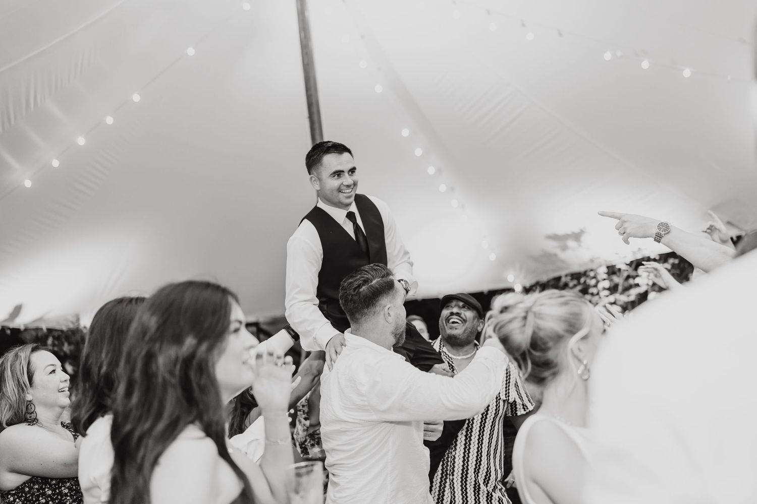 Black and white photo of wedding guests dancing and celebrating under a tent.