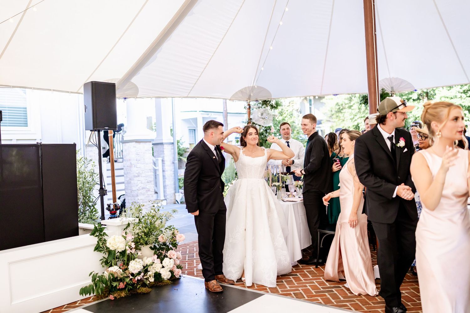 Wedding celebration under an elegant white tent with floral arrangements and formal attire.