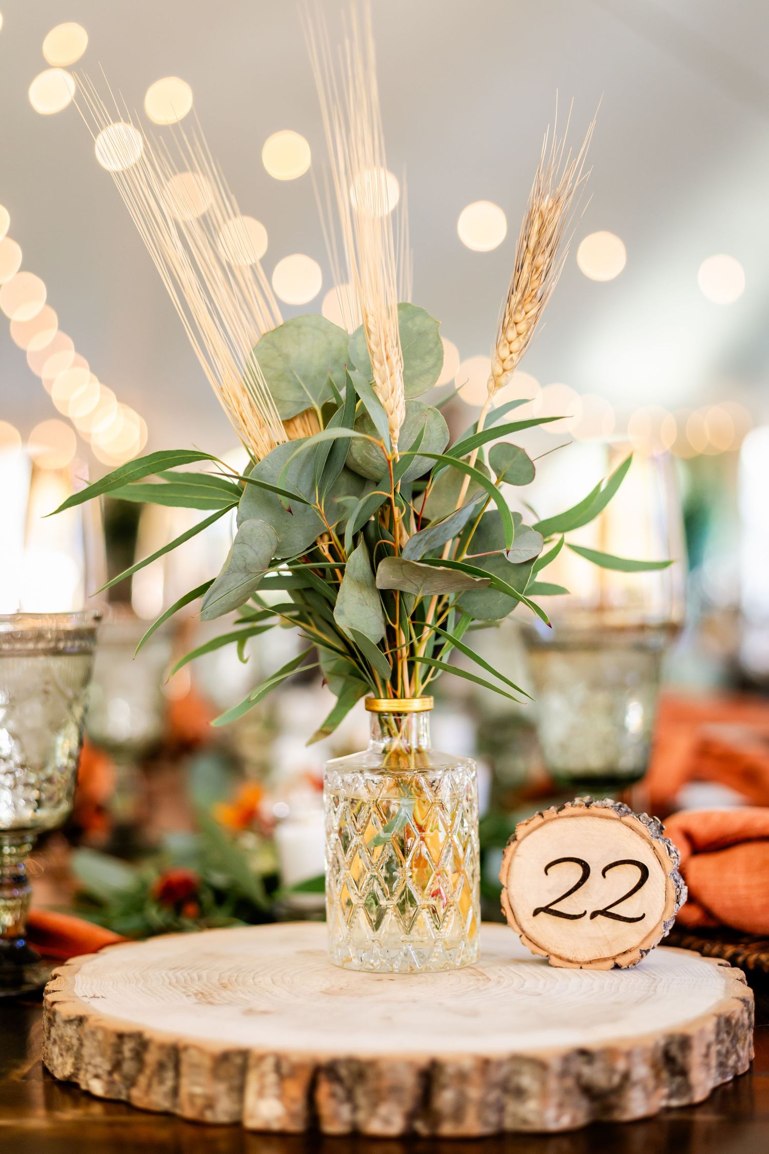 Rustic wedding table decor with wood slices, wheat stems and greenery centerpieces.