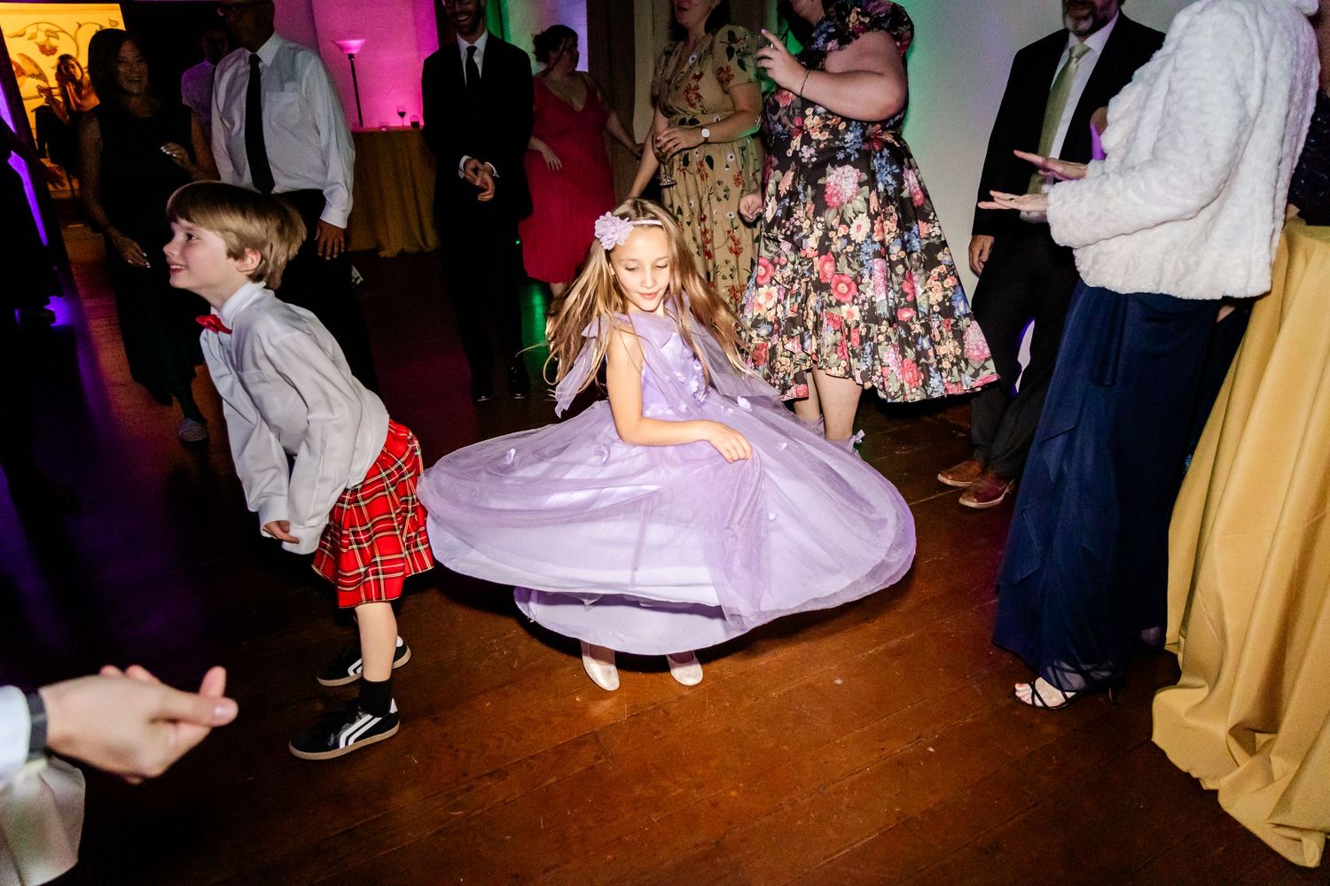 Children dancing at a wedding reception with a girl twirling in a purple dress.