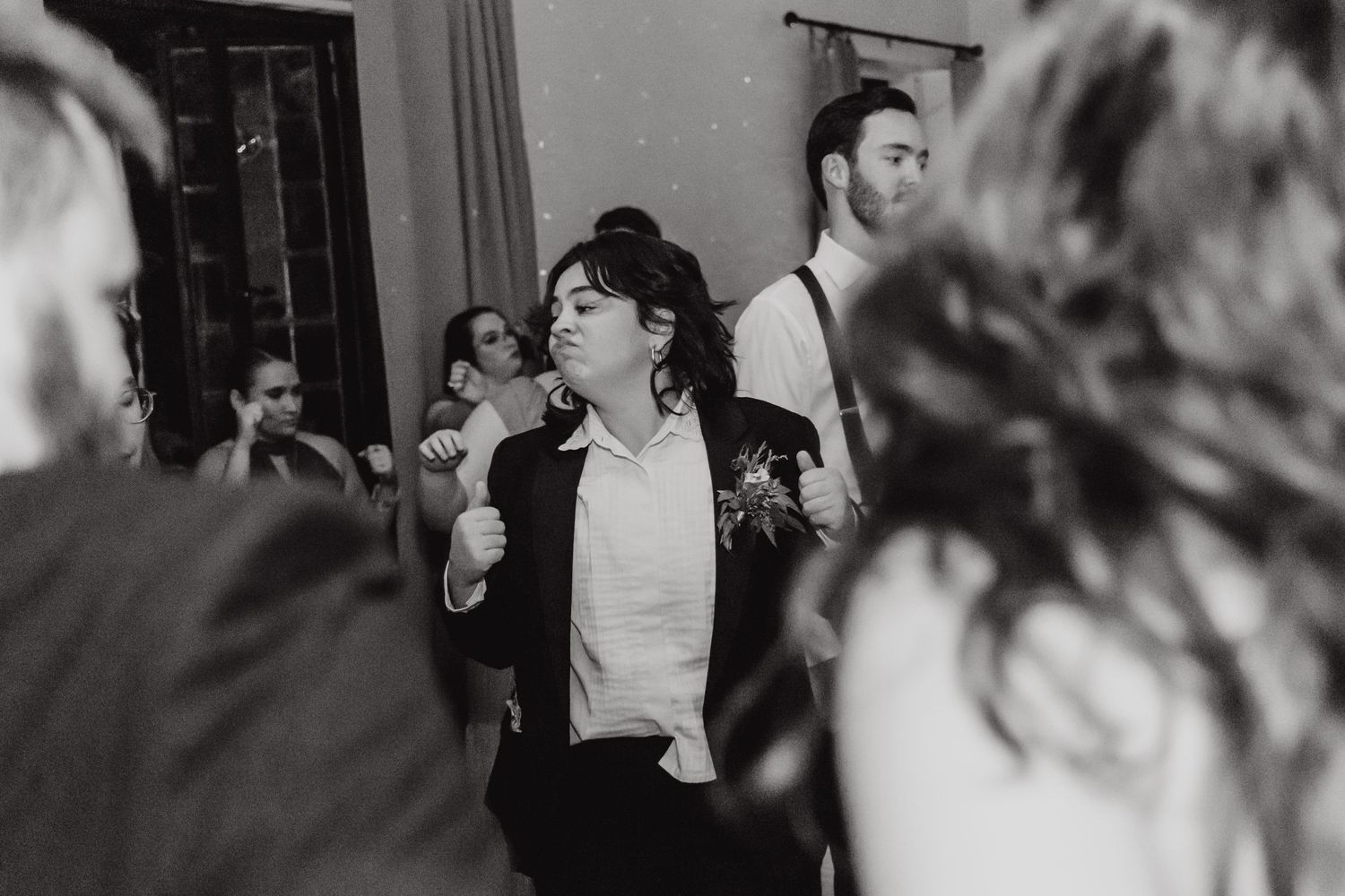 A black and white candid photo of wedding reception guests dancing and celebrating.